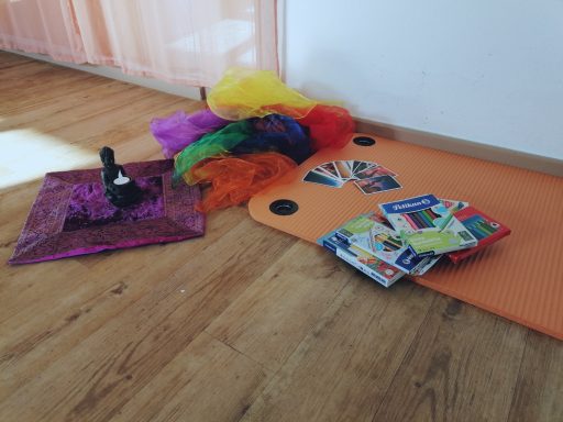 Bunte Tücher und Zeitschriften liegen auf einem Holzboden neben einer orangefarbenen Matte.