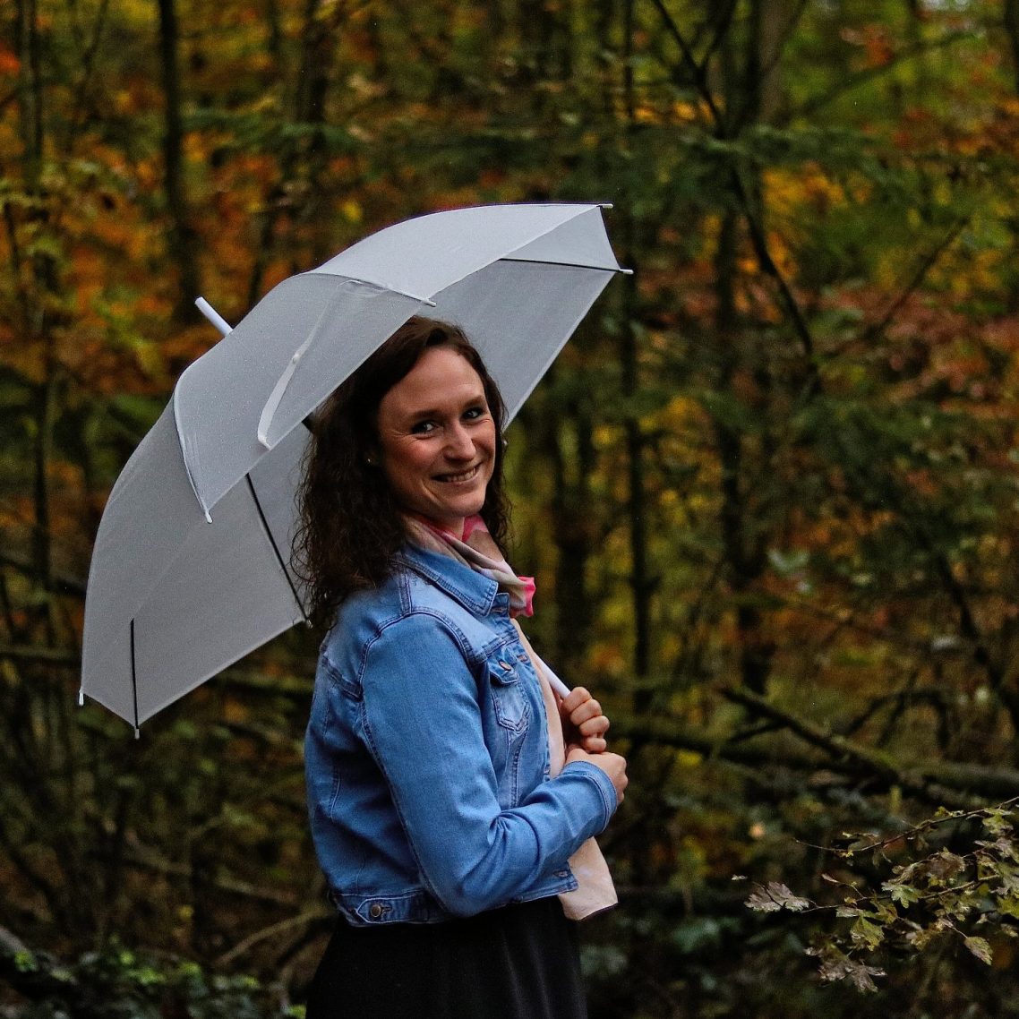 Frau mit Regenschirm steht in einem herbstlichen Wald.