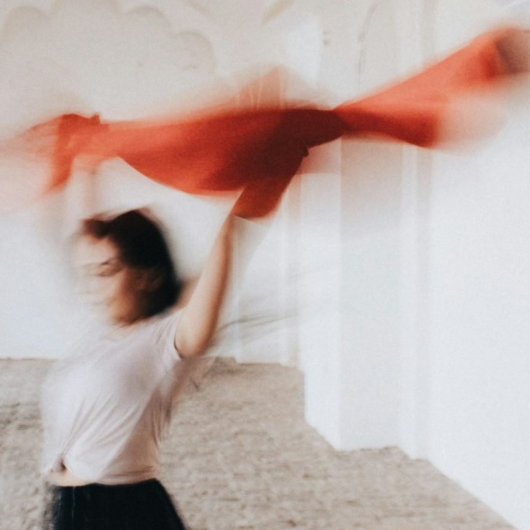 Frau mit rotem Tuch, das sie in einem hellen Raum schwingt, Hintergrund verschwommen.