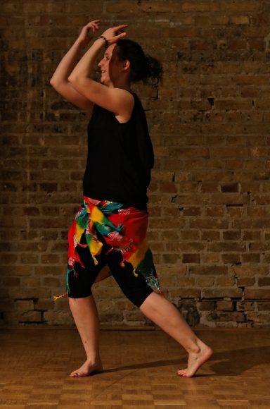 Schwungvoll von afrikanischer Musik inspiriert sind zwei tanzende Beine erkennbar. Die Person trägt ein buntes Tuch um die Hüfte.