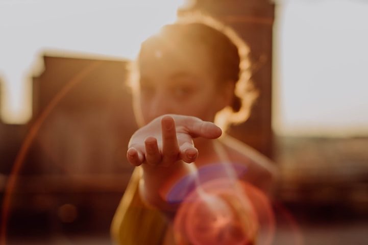 Frau streckt die Hand aus, Sonnenlicht hinter ihr erzeugt einen warmen, leuchtenden Effekt.