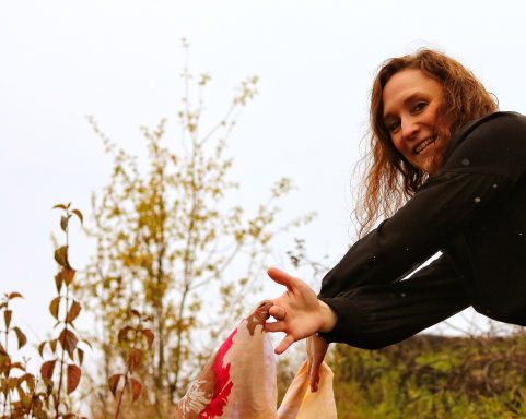 Frau mit braunen Haaren hält einen roten und gelben Stoff in der Natur.